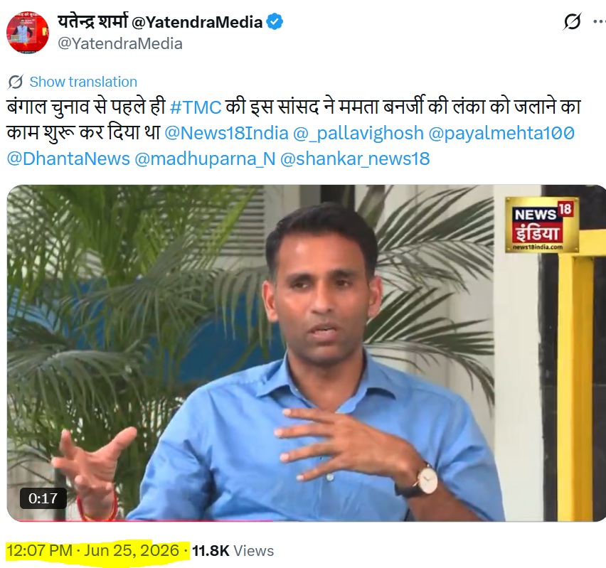 Man in a blue shirt speaks and gestures with his hands, seated outdoors with green plants in the background; News18 India logo visible in the top-right corner.