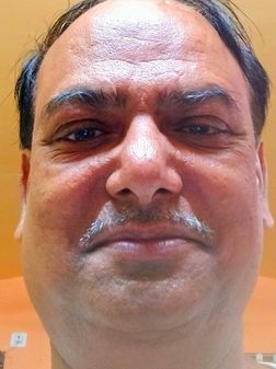 Close-up of a middle-aged man's face with a mustache, looking at the camera against an orange wall.