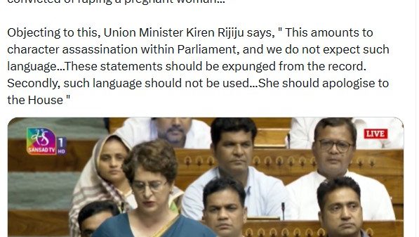 A woman in a blue sari speaking at a Parliament session, with other MPs seated behind.