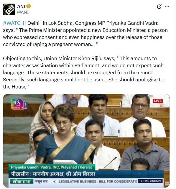 A woman in a blue sari speaking at a Parliament session, with other MPs seated behind.
