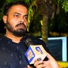 Man with a beard in a dark kurta speaks into a microphone during an outdoor interview at night.