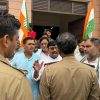 Group of men gathered outside a building, Indian flags raised, police in tan uniforms in the foreground.