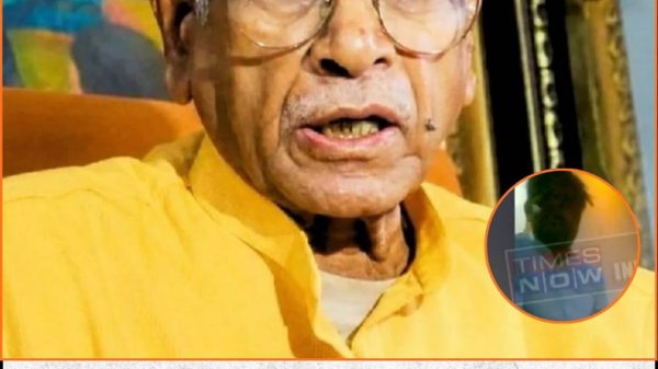 Senior Indian man with orange tilak and round glasses wearing a yellow kurta, speaking in a Times Now news segment; Times Now watermark visible.