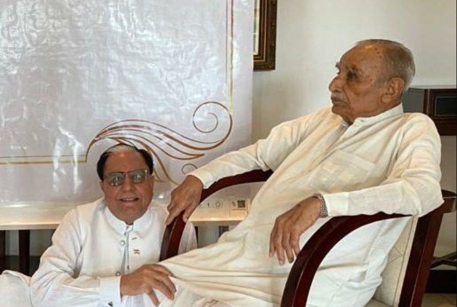 chandra_goenka | No. 1 Indian Media News Portal Two elderly men in white traditional outfits sit together indoors, one in a chair and the other leaning nearby.