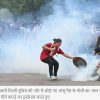 Young woman in a red shirt throws or hands a bottle toward a protester with a shield amid tear gas at a street demonstration.