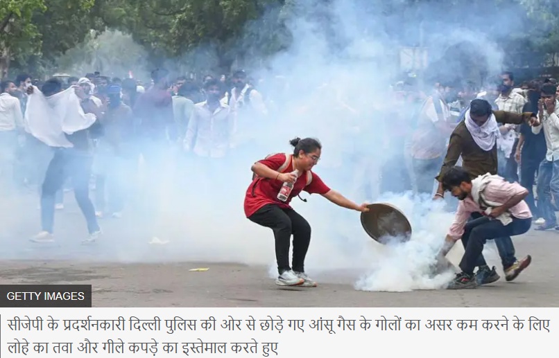 Young woman in a red shirt throws or hands a bottle toward a protester with a shield amid tear gas at a street demonstration.