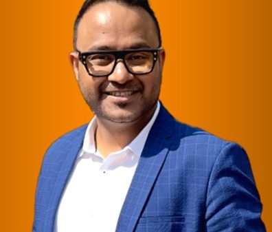 Smiling man in a blue blazer and white shirt wearing glasses, against an orange background.