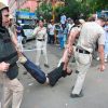 Police officers in beige uniforms and protective gear restrain a man being dragged by his arms while onlookers watch on a city street