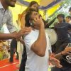 A man in a white t-shirt is on his phone while being surrounded by people under a yellow canopy at an outdoor event.