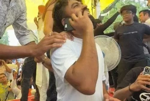 A man in a white t-shirt is on his phone while being surrounded by people under a yellow canopy at an outdoor event.