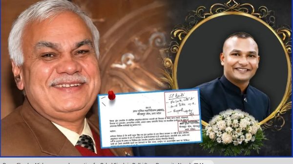 Smiling older man in a brown suit holding a document pinned with a red pushpin; to the right is a decorative framed portrait of a younger man with a bouquet of white flowers.