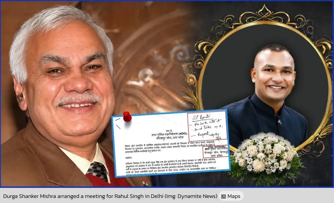 Smiling older man in a brown suit holding a document pinned with a red pushpin; to the right is a decorative framed portrait of a younger man with a bouquet of white flowers.