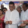 Man in a white shirt cuts a red ribbon at a ribbon-cutting ceremony, surrounded by smiling colleagues and guests in a festive setting.