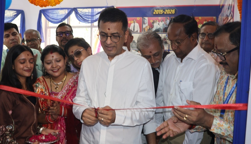 Man in a white shirt cuts a red ribbon at a ribbon-cutting ceremony, surrounded by smiling colleagues and guests in a festive setting.
