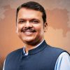 Smiling man in a blue Nehru jacket against an orange map of India backdrop.