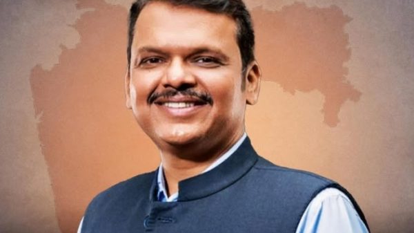 Smiling man in a blue Nehru jacket against an orange map of India backdrop.