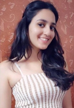 Young woman with long dark hair smiling at the camera, wearing a striped sleeveless top, in front of an orange patterned wall.