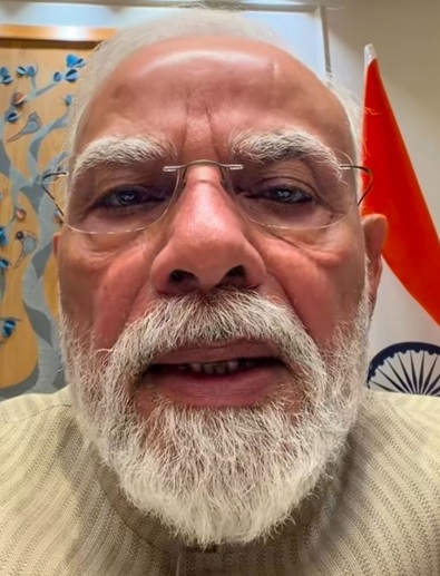 Close-up of an elderly man with a white beard and glasses taking a selfie, with an Indian flag visible in the background.