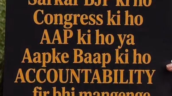 A protest sign in orange and white text demanding accountability from any party, held in front of a person outdoors.