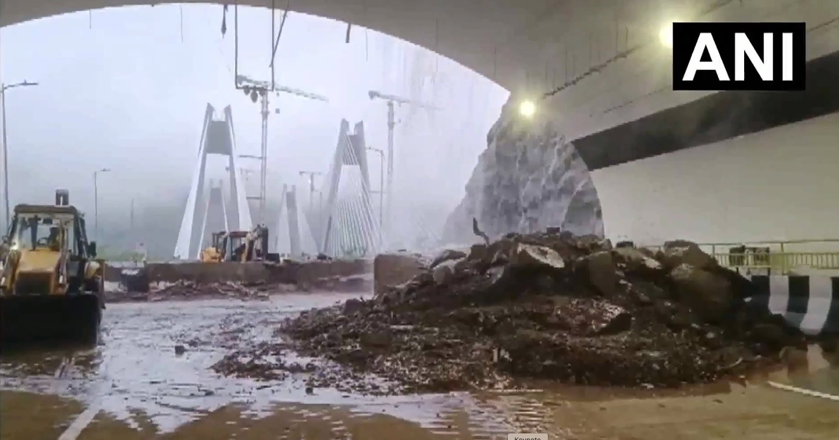Construction site inside a curved tunnel with muddy floor, excavators, and a large pile of dirt in the foreground; structural framework visible in the distance