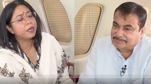 Two people seated in a private jet; a woman in a floral shawl speaks while a man with a microphone listens.