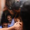 Crowded scene of men helping a man on the ground, several arms grip his limbs in a tense moment.