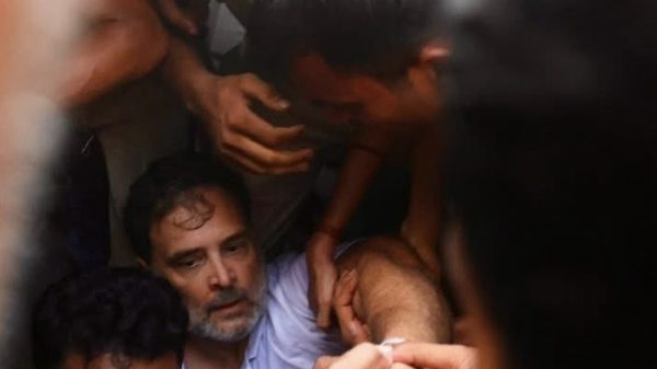Crowded scene of men helping a man on the ground, several arms grip his limbs in a tense moment.