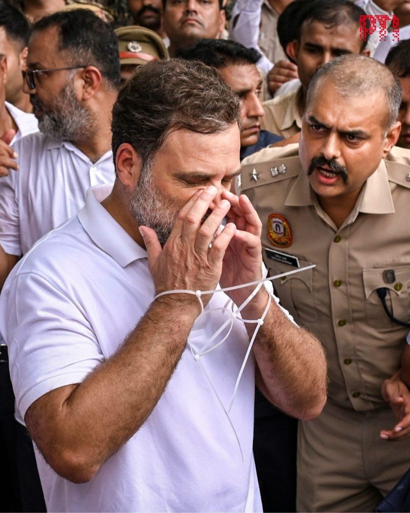 img_9868 | No. 1 Indian Media News Portal Man in a white shirt covers his face with his hands while surrounded by a crowd, with a police officer in khaki beside him.