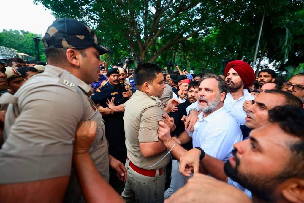Crowd confronts police officers gripping a man in uniform during a tense outdoor clash.