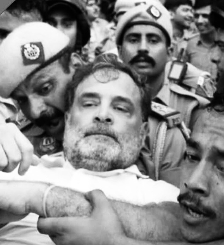 Man with a beard being restrained by police officers in a crowded scene (black and white).