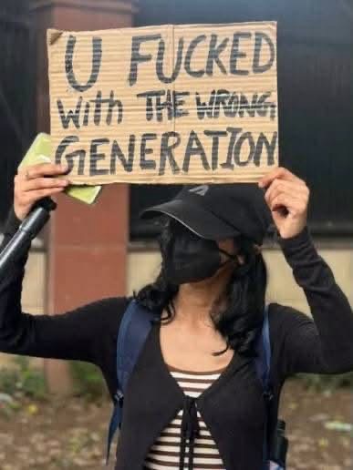 img_9938 | No. 1 Indian Media News Portal Person wearing a dark cap, black mask, and backpack holds up a cardboard sign that reads 'U Fucked with the wrong generation'.