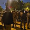 Nighttime street scene with a large crowd of civilians and uniformed officers facing each other, suggesting a protest or crowd-control event on a city street.