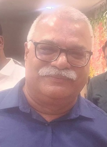 Portrait of a middle-aged man with gray hair and a mustache wearing glasses and a blue shirt, smiling at the camera.