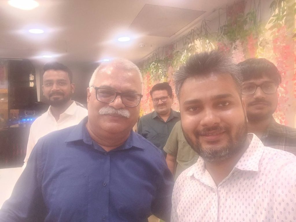 indu shekhar_3 | No. 1 Indian Media News Portal Four men pose for a group selfie indoors, with colorful floral decor in the background.