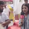 Female reporter holding a pink microphone interviewing a man with arms folded at an outdoor event.