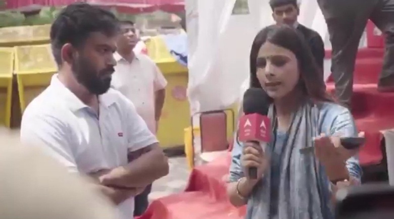 Female reporter holding a pink microphone interviewing a man with arms folded at an outdoor event.