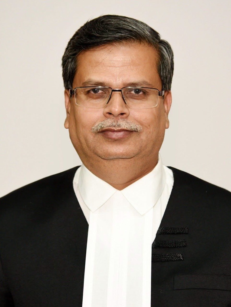 Head-and-shoulders portrait of a middle-aged man in a black suit and white shirt, wearing glasses, looking at the camera.