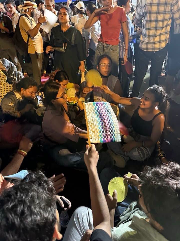 jantar_mantar_1 | No. 1 Indian Media News Portal Crowd of people sitting cross‑legged in a circle, weaving a colorful textile together at a festival or market.
