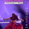 Singer in a red floral outfit twirls on a purple-lit stage, microphone in hand; event banner reads 'Dehradun Jasmine Sandlas' 'Pride Ground' '17th July'