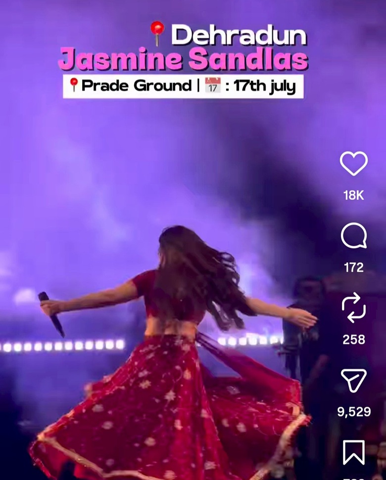 Singer in a red floral outfit twirls on a purple-lit stage, microphone in hand; event banner reads 'Dehradun Jasmine Sandlas' 'Pride Ground' '17th July'