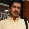 Portrait of a man with a mustache wearing a light yellow kurta, standing outdoors with a shoulder bag strap visible.