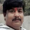 Close-up of a man with a red tilak on his forehead, outdoors near a corrugated metal fence.
