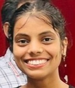 Smiling woman with dark hair tied back, wearing small earrings, against a red background.