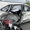 White SUV severely damaged on the driver's side from a collision, airbags deployed and interior exposed under the shattered window glass.