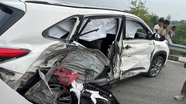 White SUV severely damaged on the driver's side from a collision, airbags deployed and interior exposed under the shattered window glass.