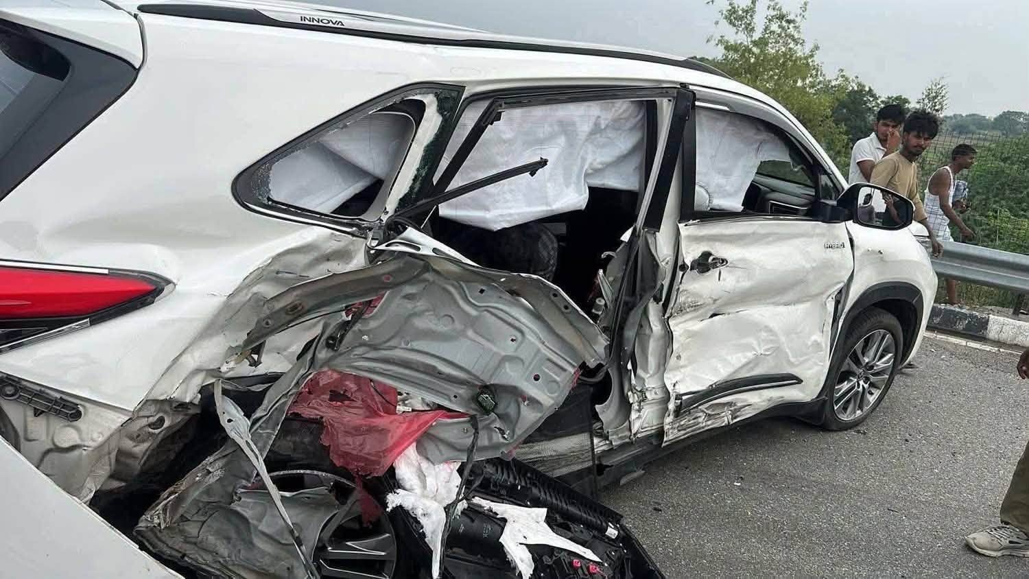 White SUV severely damaged on the driver's side from a collision, airbags deployed and interior exposed under the shattered window glass.