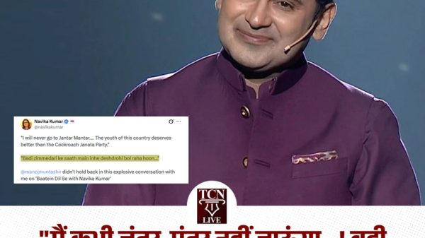 Male host on stage wearing a purple kurta with a headset microphone, smiling, with a large Hindi headline banner at the bottom.