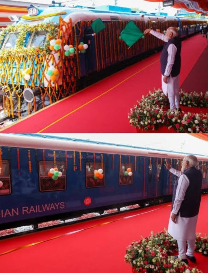 modi_train | No. 1 Indian Media News Portal VIP in traditional attire waves toward a blue Indian Railways train at a festive inauguration, with balloons and garlands on a red carpet.