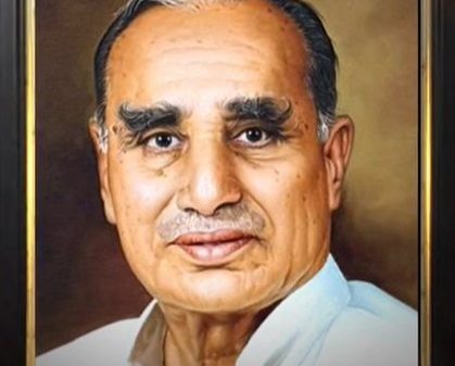 Portrait of an elderly man with white hair and thick eyebrows, wearing a light shirt, framed in a dark wood frame.
