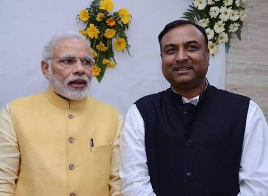 navin_modi | No. 1 Indian Media News Portal Two men posing for a photo; left man wears a yellow kurta with glasses, right man in a white shirt and dark vest, floral arrangements in the background.